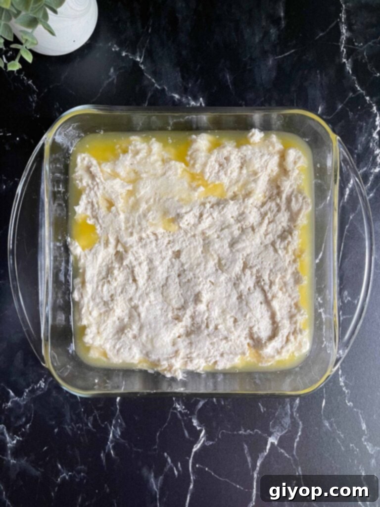 Sticky biscuit dough evenly spread over the melted butter in a square glass baking pan, ready for scoring.