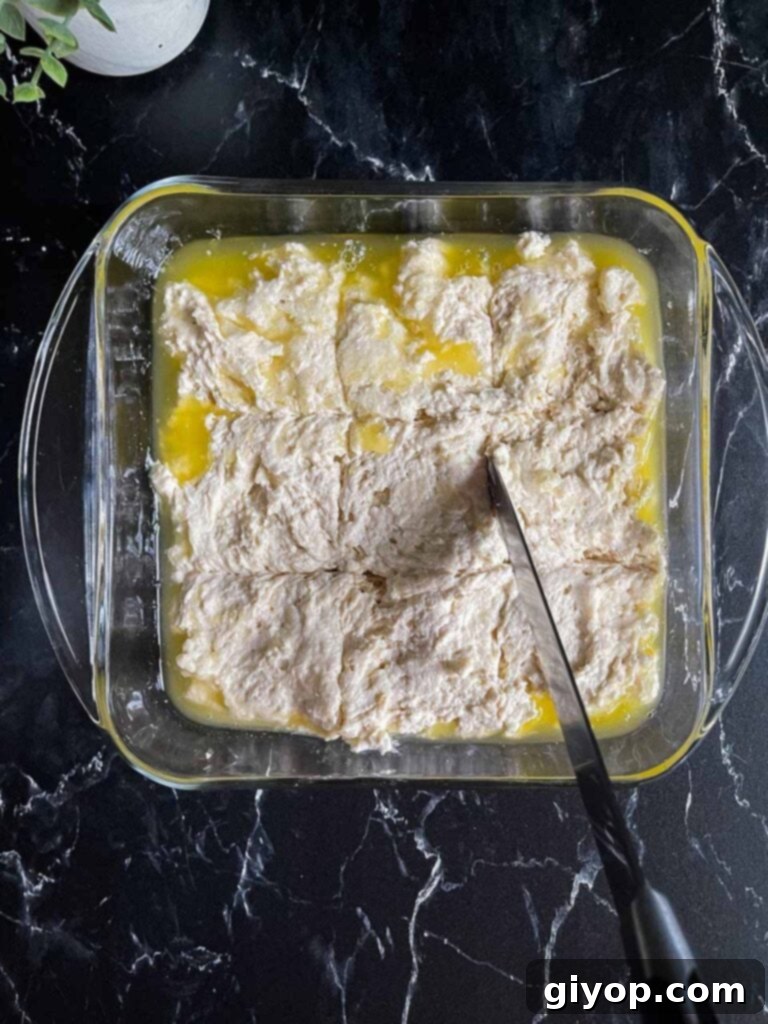 A knife gently scoring the biscuit dough into nine squares directly in the baking dish, atop a pool of melted butter.