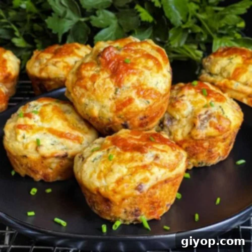 Sausage muffins stacked on a black plate garnished with diced chives, a perfect breakfast.