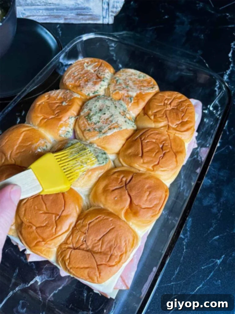 Brushing the butter mixture on top of the ham and swiss sliders.