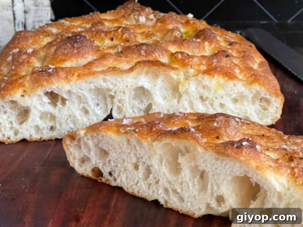 Golden-brown focaccia bread, perfectly cut in half, resting on a rustic wooden cutting board, highlighting its airy crumb.