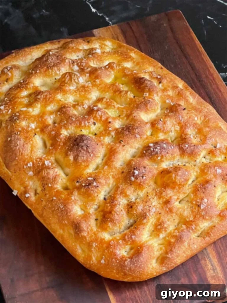 Freshly baked focaccia bread, just out of the oven, cooling on a wooden cutting board.