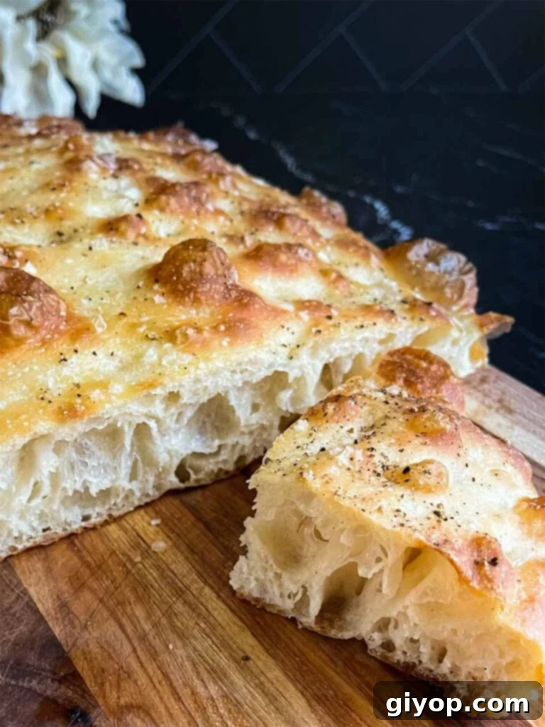 Baked overnight focaccia bread, beautifully cut into squares, on a wooden cutting board.