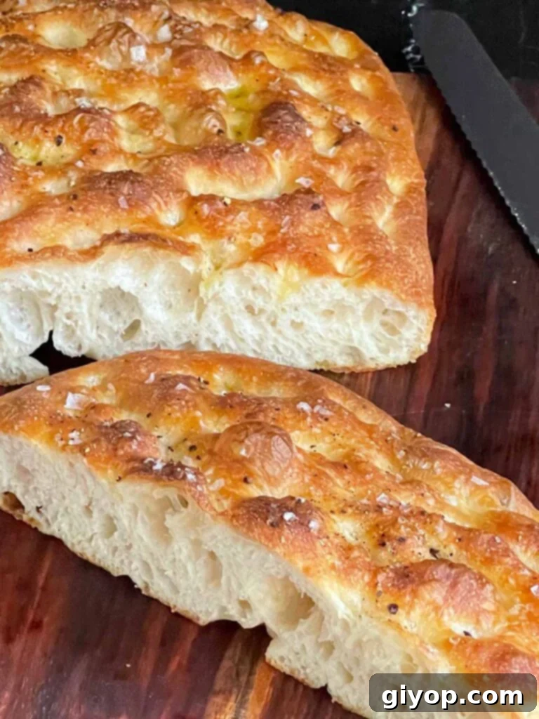 Freshly baked overnight focaccia, cut in half, showcasing its inviting texture on a wooden board.