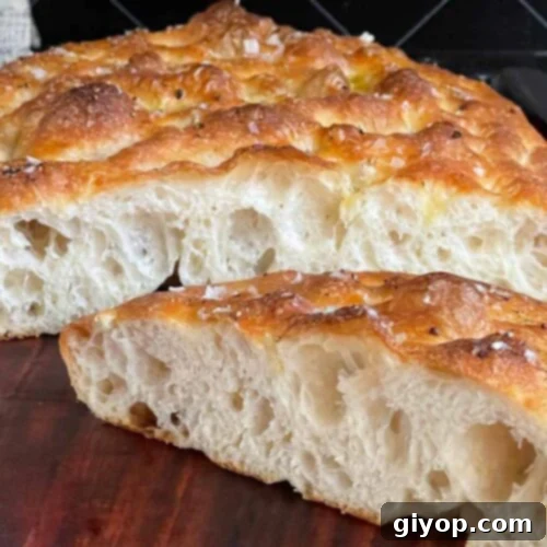 Overnight focaccia bread cut in half on a wooden cutting board.
