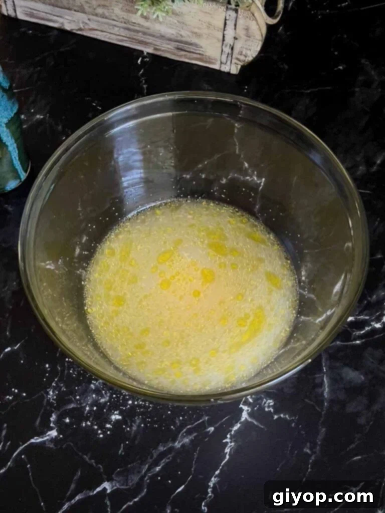 Wet ingredients for focaccia (water, yeast, olive oil, honey) mixed in a clear glass bowl.
