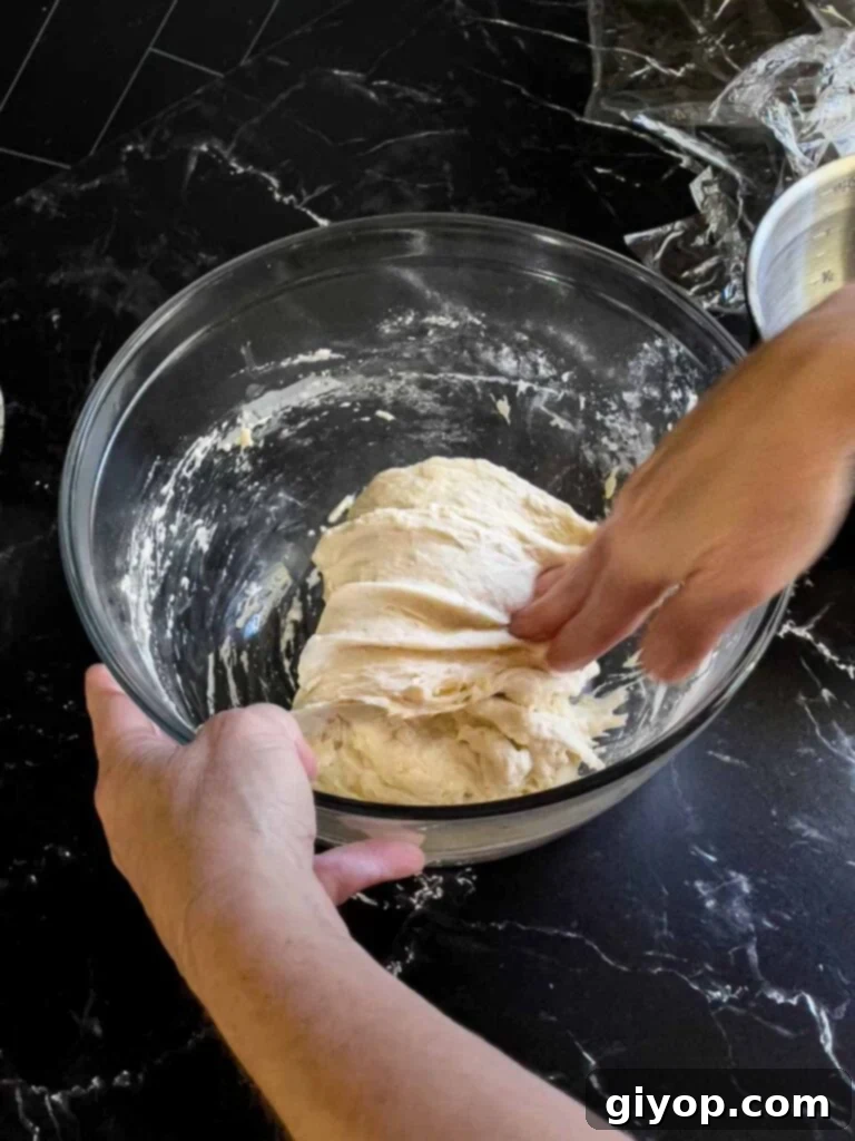 Hands stretching and folding the focaccia dough inside a glass bowl during the first round of gluten development.