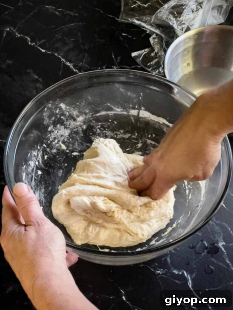 The focaccia dough undergoing its second stretch and fold in a glass bowl, becoming smoother and more elastic.