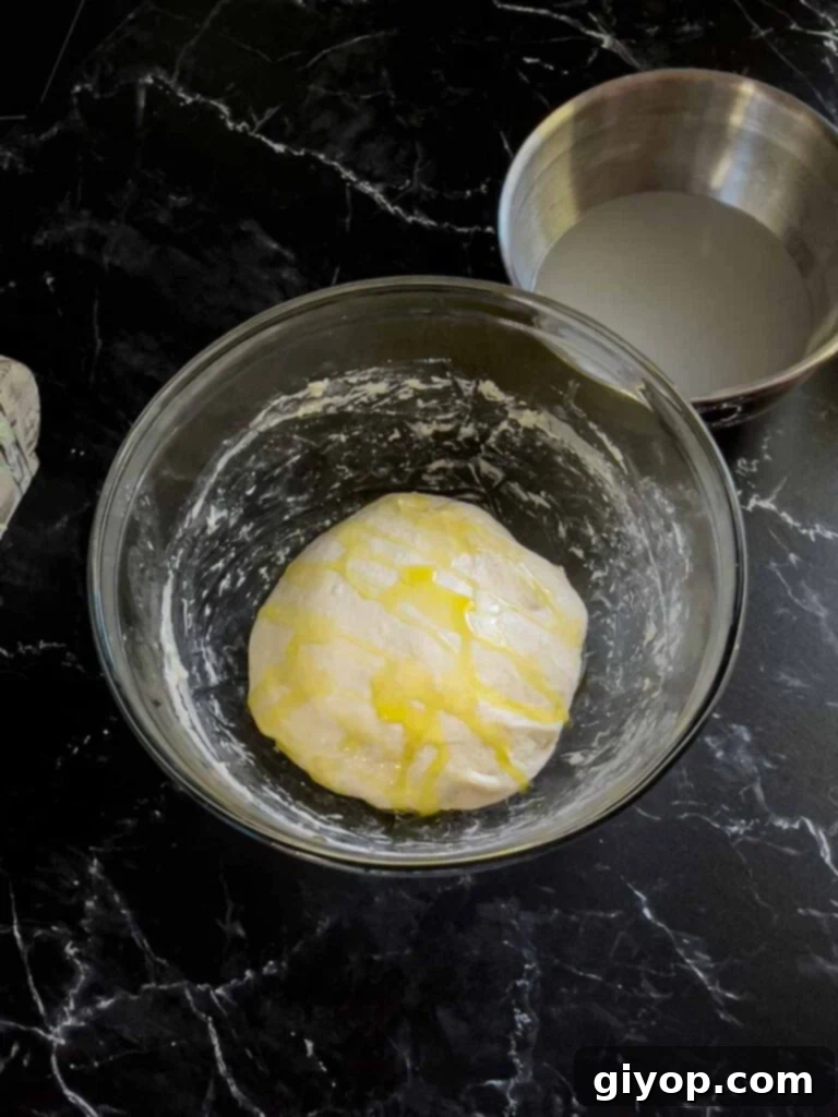 Focaccia dough liberally coated with olive oil in a glass bowl, ready for its overnight refrigeration.