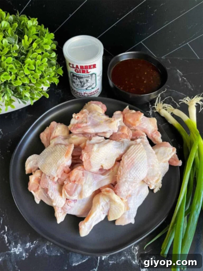 Golden Crispy Asian Oven Wings 3 Raw chicken wings on a black plate with green onions off to the side, ready for preparation.