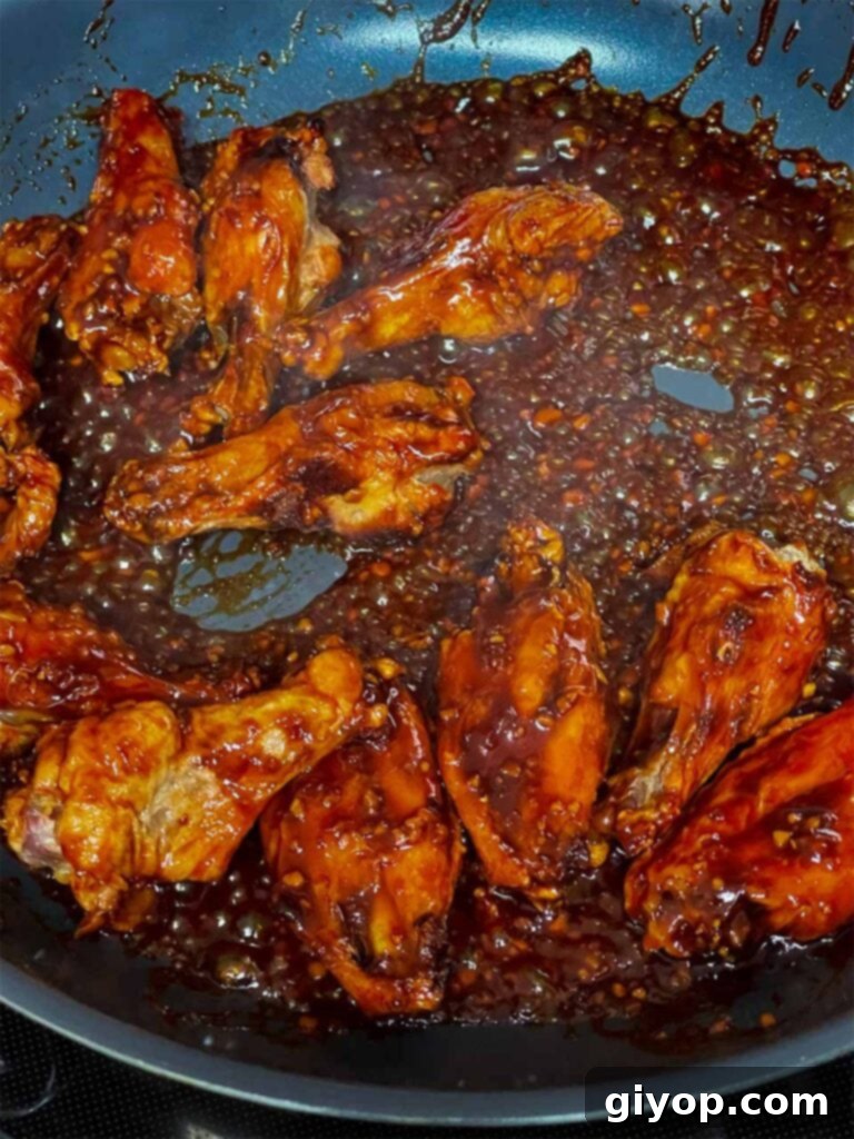 Golden Crispy Asian Oven Wings 7 Crispy chicken wings being tossed and coated in the glossy Asian dipping sauce within a hot skillet.