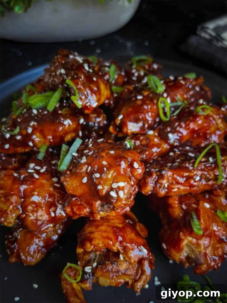 Golden Crispy Asian Oven Wings 8 A stunning plate of Asian chicken wings, generously garnished with vibrant green onions and toasted sesame seeds.