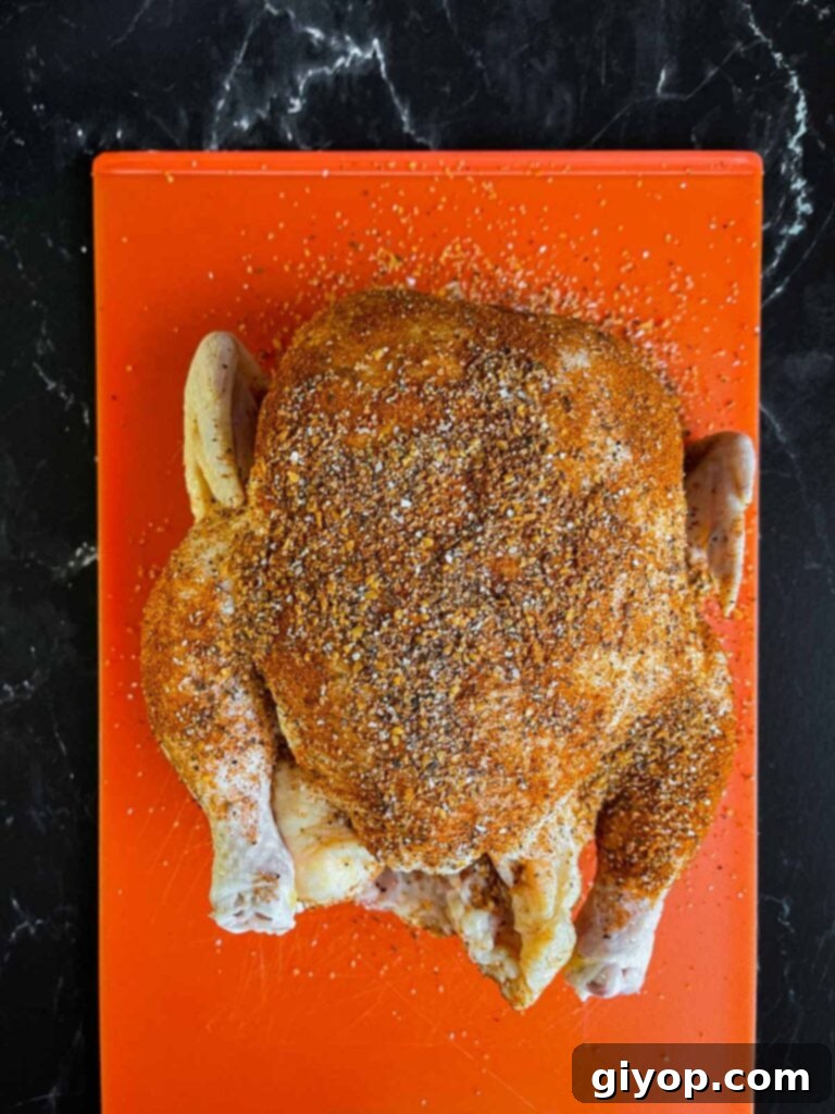Whole chicken on a plastic cutting board, generously rubbed in spices and ready for the slow cooker.