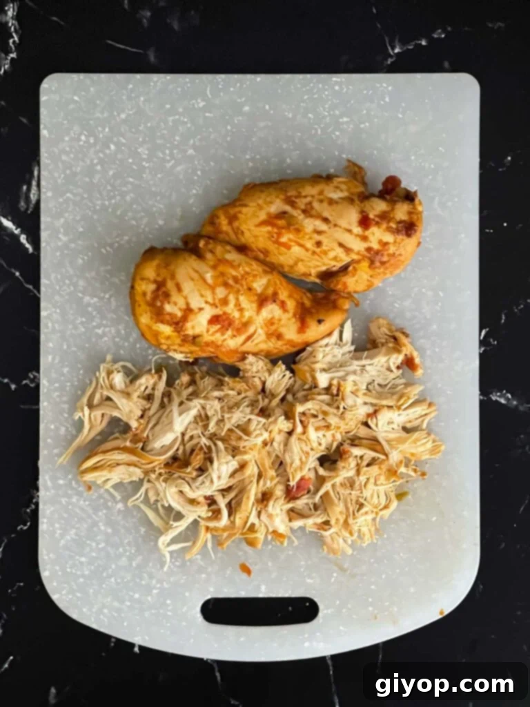 Shredded Mexican chicken on a plastic cutting board on a dark surface.