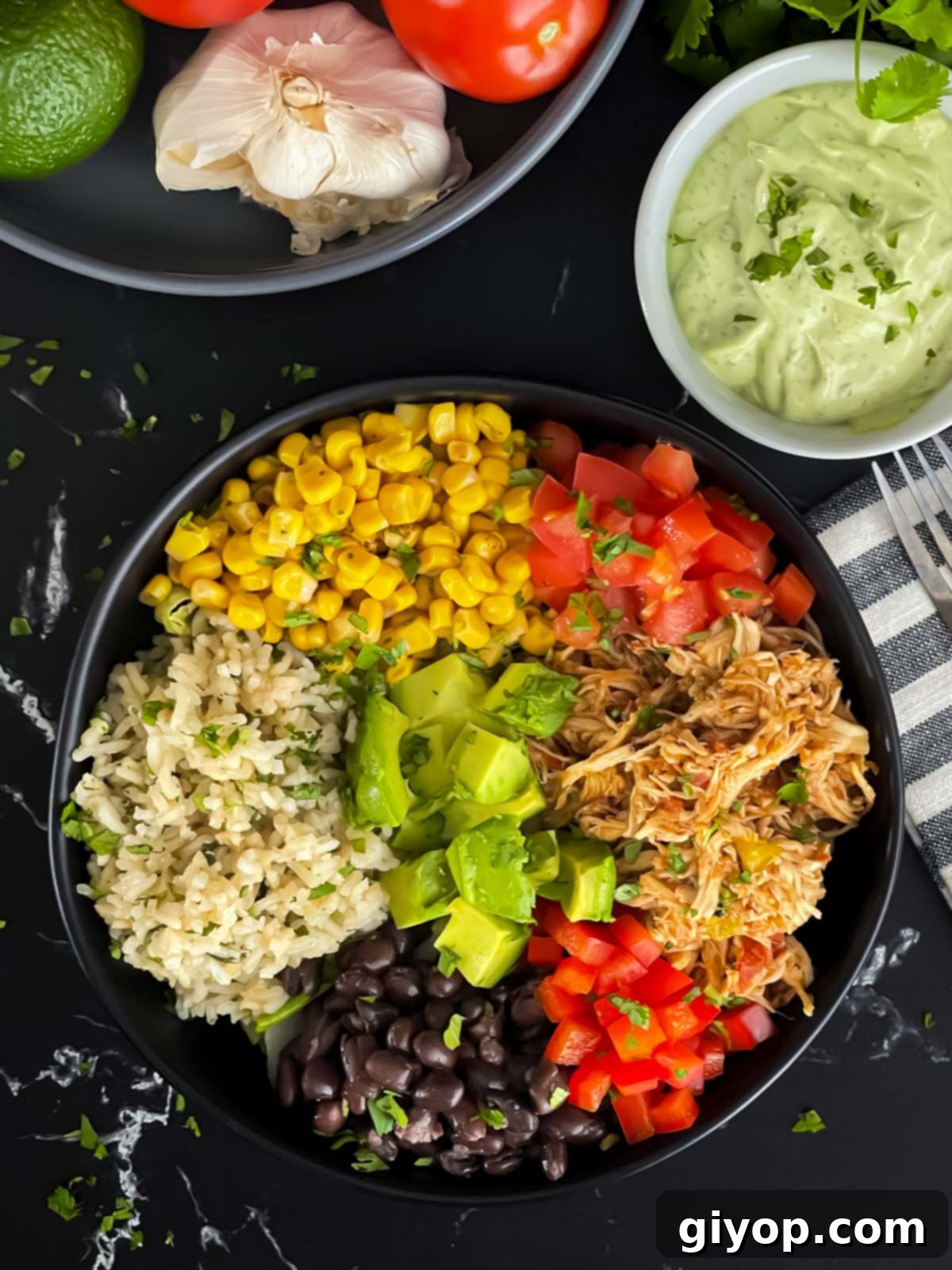 A vibrant and fully loaded chicken burrito bowl, featuring tender chicken, rice, beans, corn, and creamy avocado sauce, artfully arranged on a dark background.
