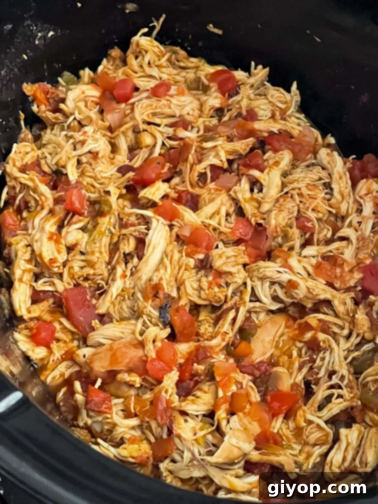 Perfectly shredded Mexican chicken simmering in its rich, spiced sauce within the crock of a slow cooker, ready for burrito bowls.