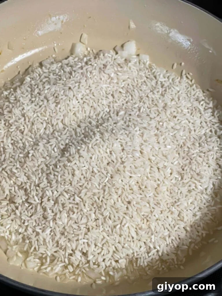 White rice being added to sautéed onions in a skillet, showcasing the initial step of toasting the rice for a flavorful base.