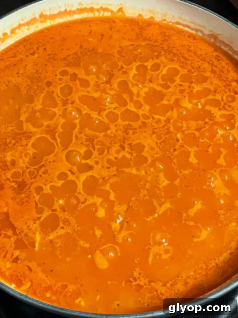 Vibrant Mexican red rice cooking in a skillet, covered and simmering gently, nearing completion.