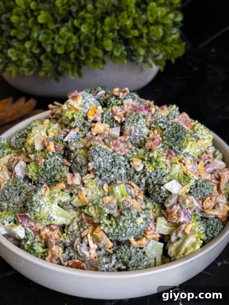 A beautifully presented bowl of creamy broccoli salad, garnished with fresh herbs, against a light background.