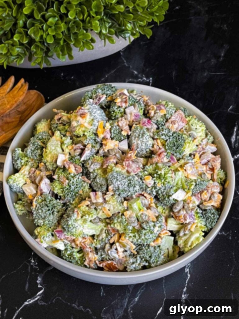 A serving of homemade broccoli salad in a elegant light-colored bowl, with a soft-focus plant in the background, hinting at freshness.