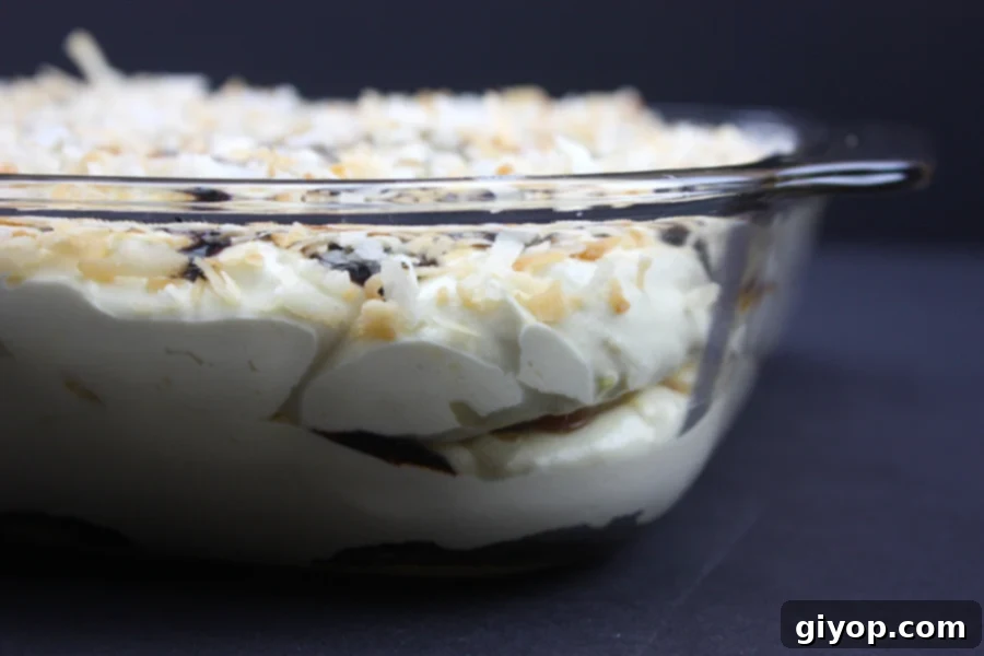 The completed Samoa Cake in a glass baking dish, with all layers assembled and a generous topping of toasted coconut, caramel, and chocolate, ready for chilling.