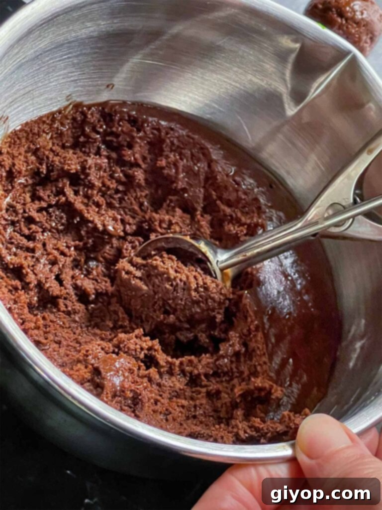 Chilled chocolate crinkle cookie dough being portioned into uniform balls with a cookie scoop.
