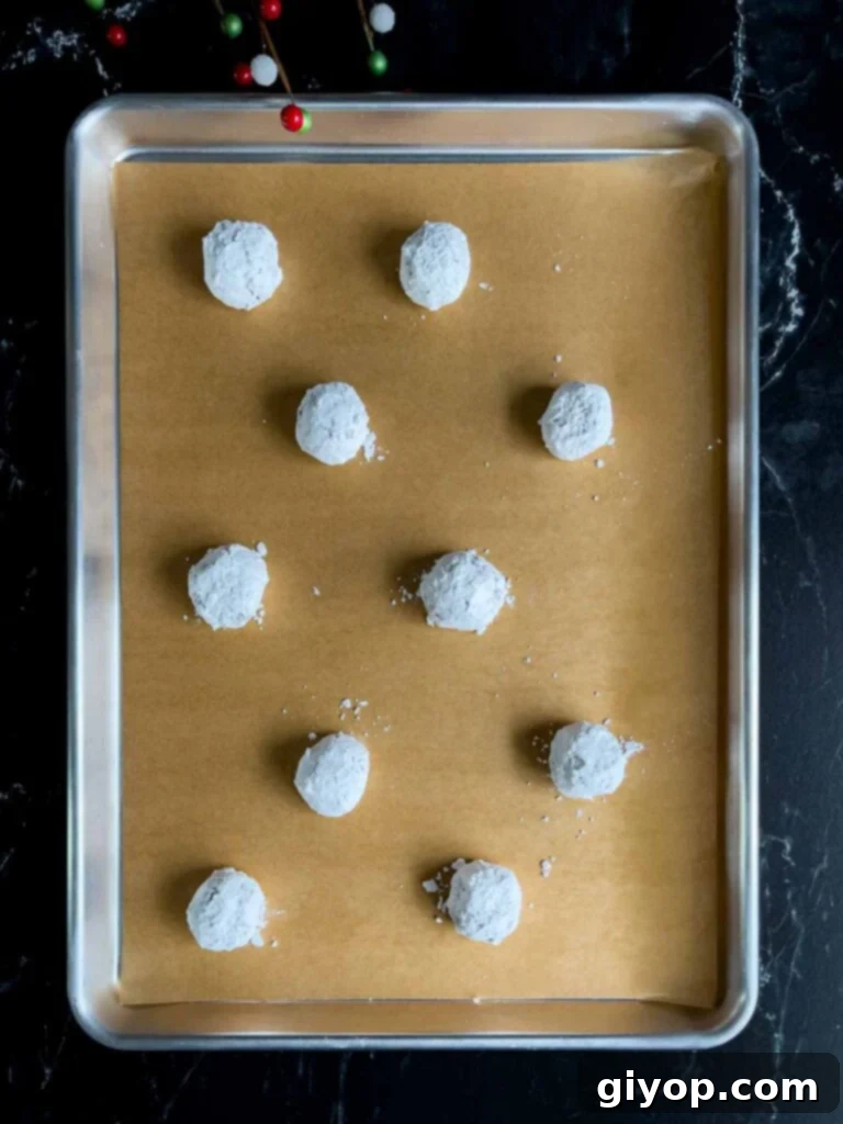Neatly arranged chocolate crinkle cookie dough balls, generously coated in powdered sugar, on a parchment-lined baking sheet, ready for the oven.