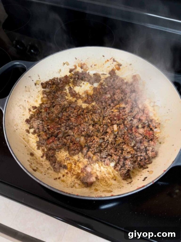 Cooked ground beef with spices cooking in a cast iron skillet.