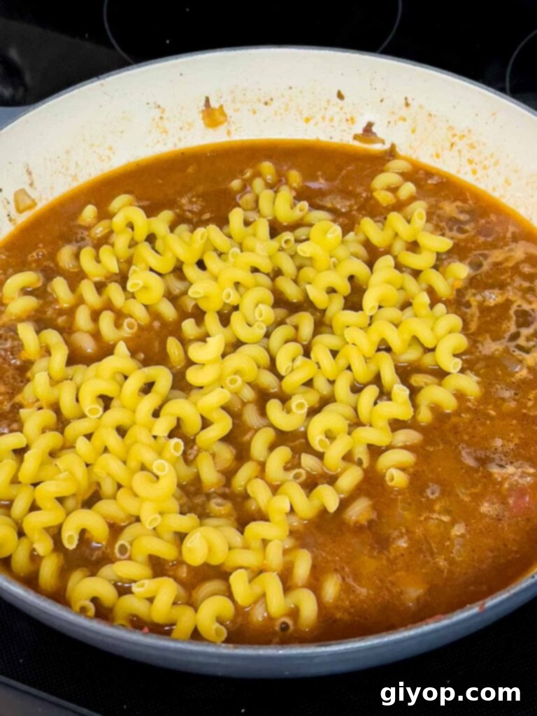 Uncooked pasta just added to beef stock in a cast iron skillet.