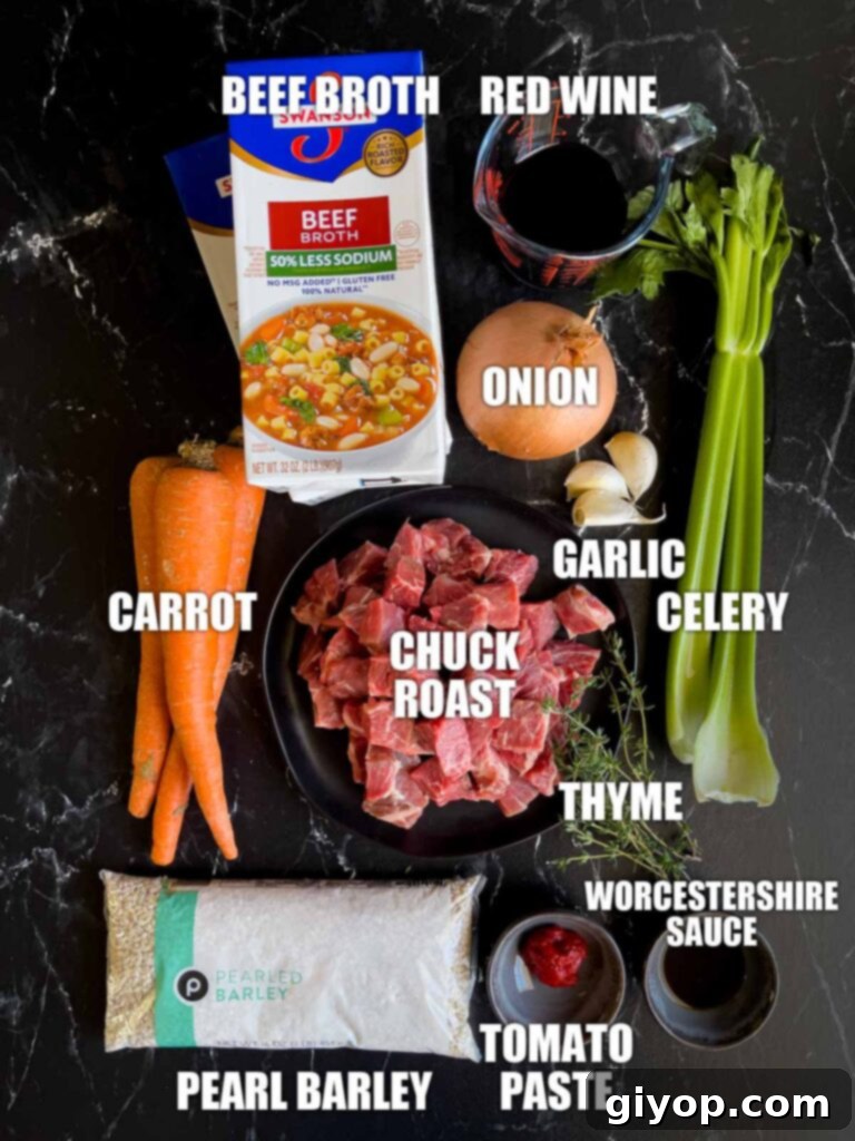 A collection of fresh ingredients laid out on a dark surface, including cubed beef, chopped carrots, celery, and onions, garlic, thyme, and pearl barley, for making beef barley soup.