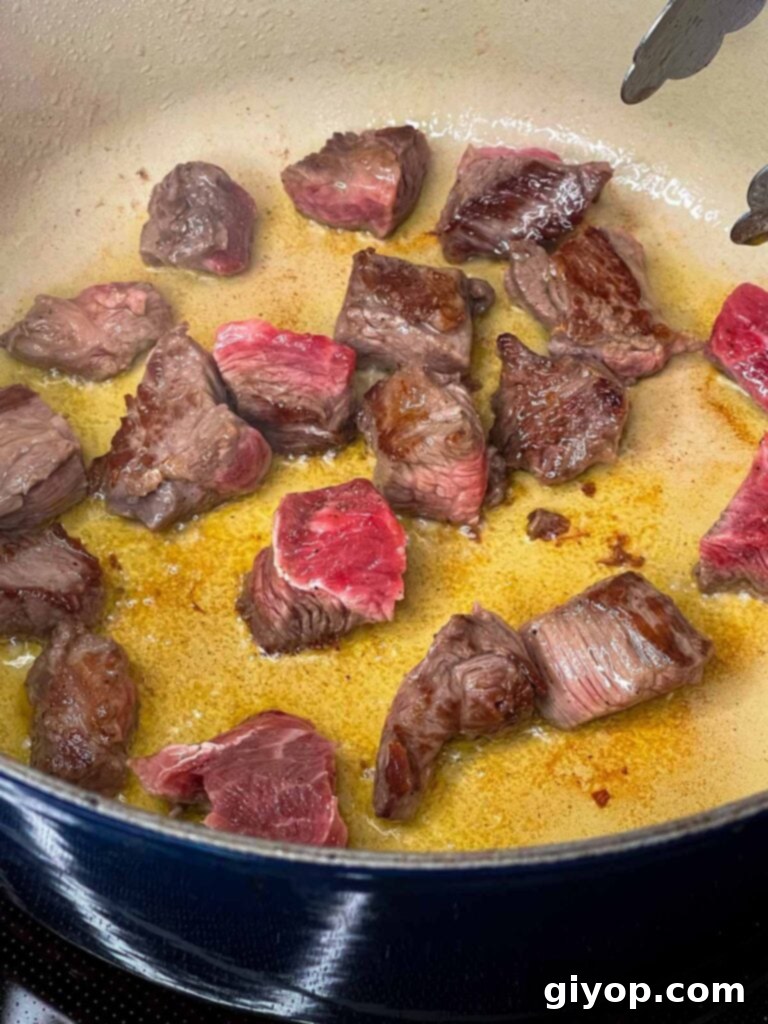 Cubed stew meat being browned in a large cast-iron Dutch oven on a stovetop, creating a delicious crust.