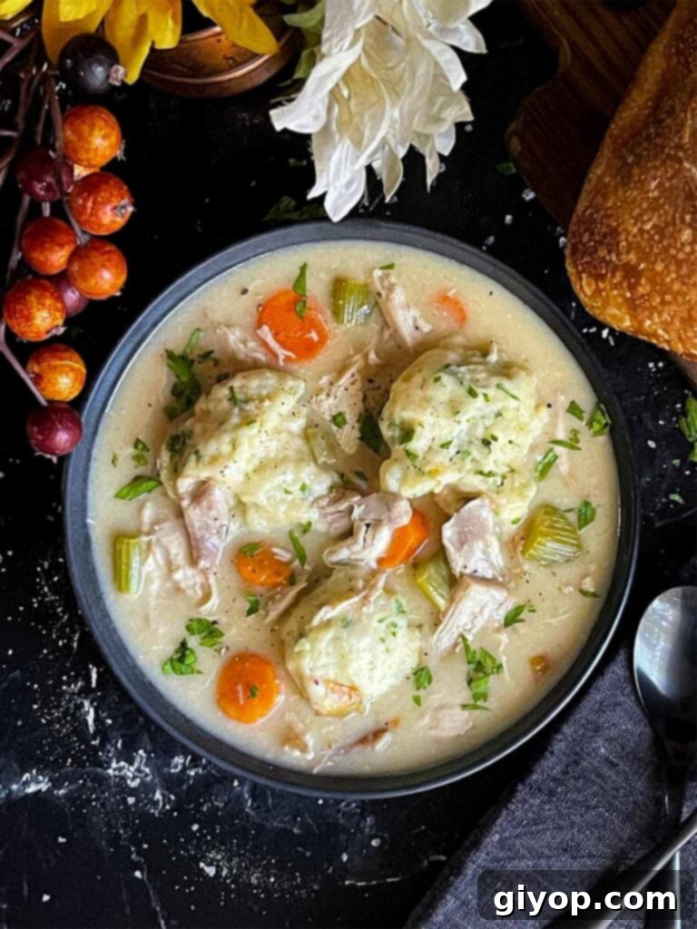 Homemade chicken and dumplings in a dark bowl, ready to be served, with a rustic loaf of bread in the background.