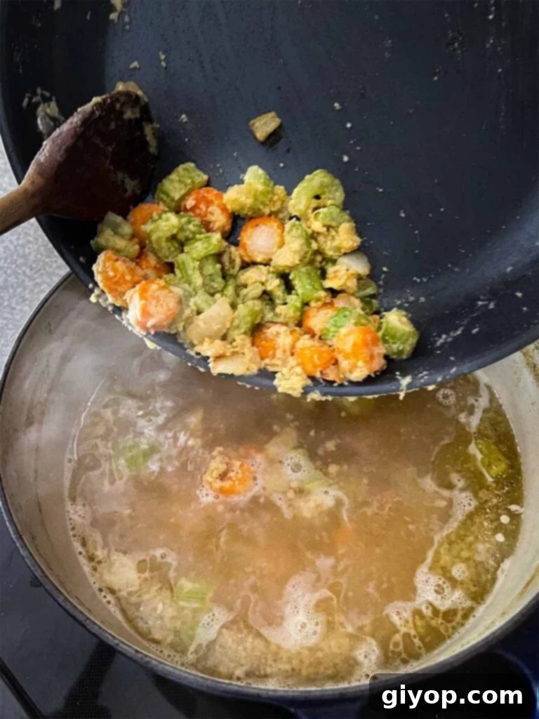 Sautéed vegetables coated in flour to form a roux, being gently added to the simmering homemade chicken stock.