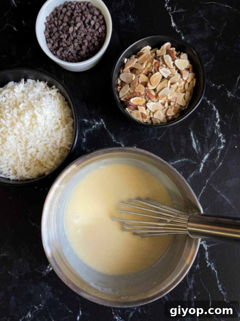 Sweetened condensed milk being mixed with cream of coconut in a metal bowl with a whisk.