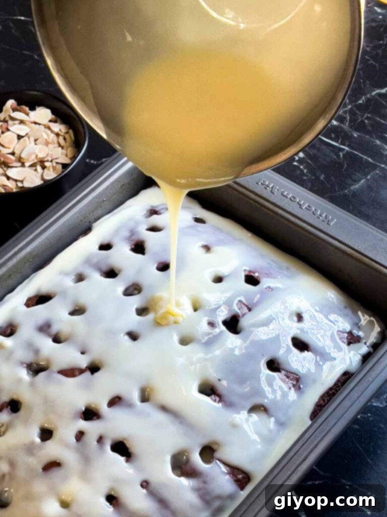 The milky coconut mixture being poured over the hot chocolate poke cake with holes visible on the surface.