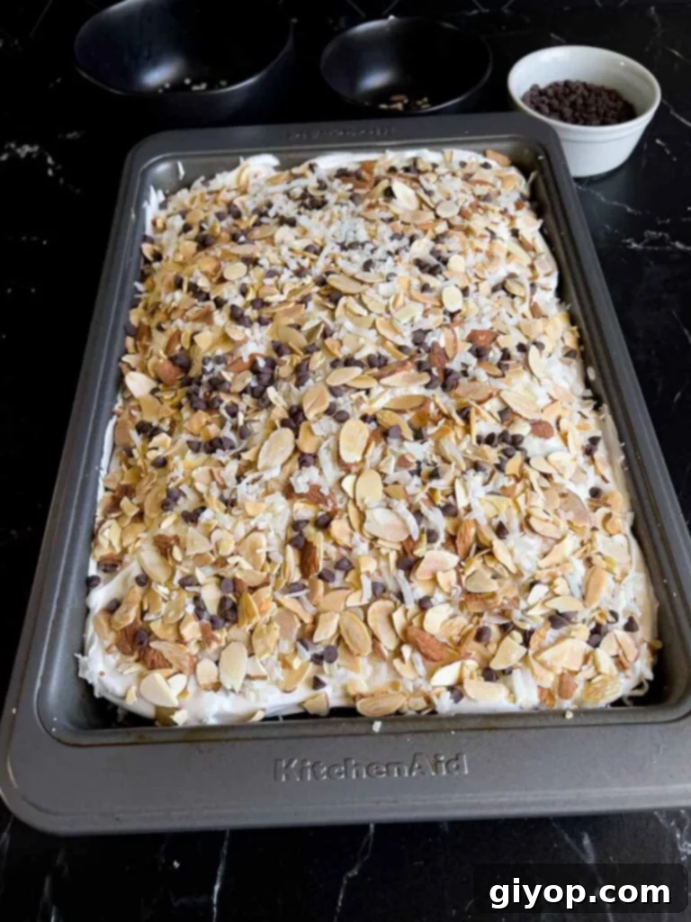 The finished Almond Joy cake with whipped topping, sprinkled with shredded coconut, sliced almonds, and mini chocolate chips.