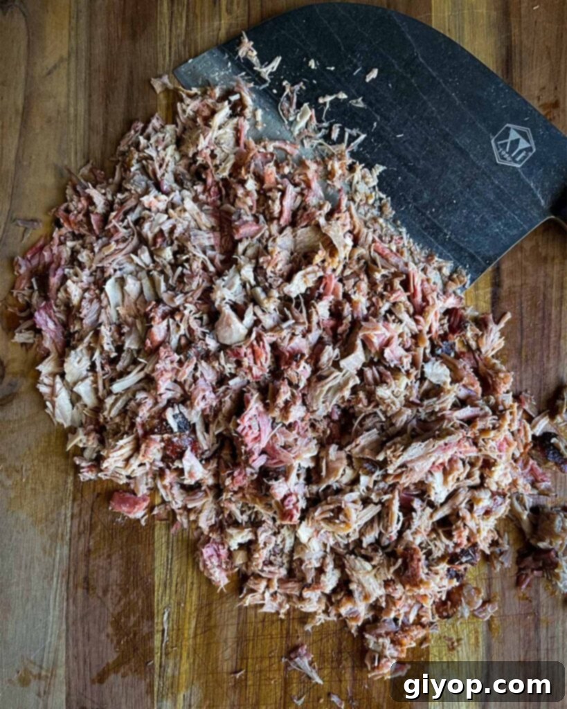 Pork butt, chopped, on a wooden cutting board with a large knife.