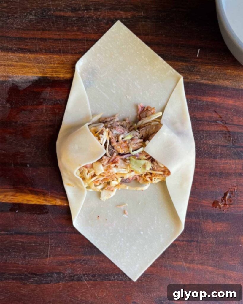 Folding the edges of the egg roll wrapper over the redneck egg roll mixture.