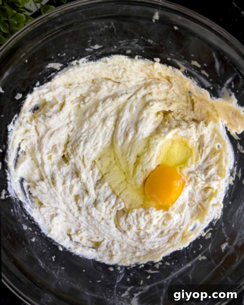 Room temperature eggs being gently added one at a time to the cannoli cheesecake mixture in a glass bowl, ensuring smooth incorporation.