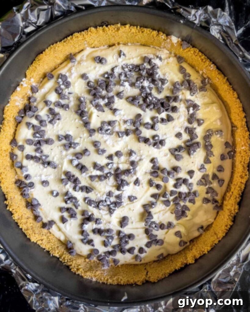Cannoli cheesecake batter layered over the cooled crust in a springform pan, with a sprinkle of chocolate chips visible between layers.