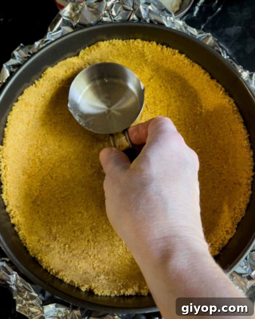 The graham cracker crust firmly pressed into the bottom and slightly up the sides of a springform pan using a metal measuring cup for an even base.