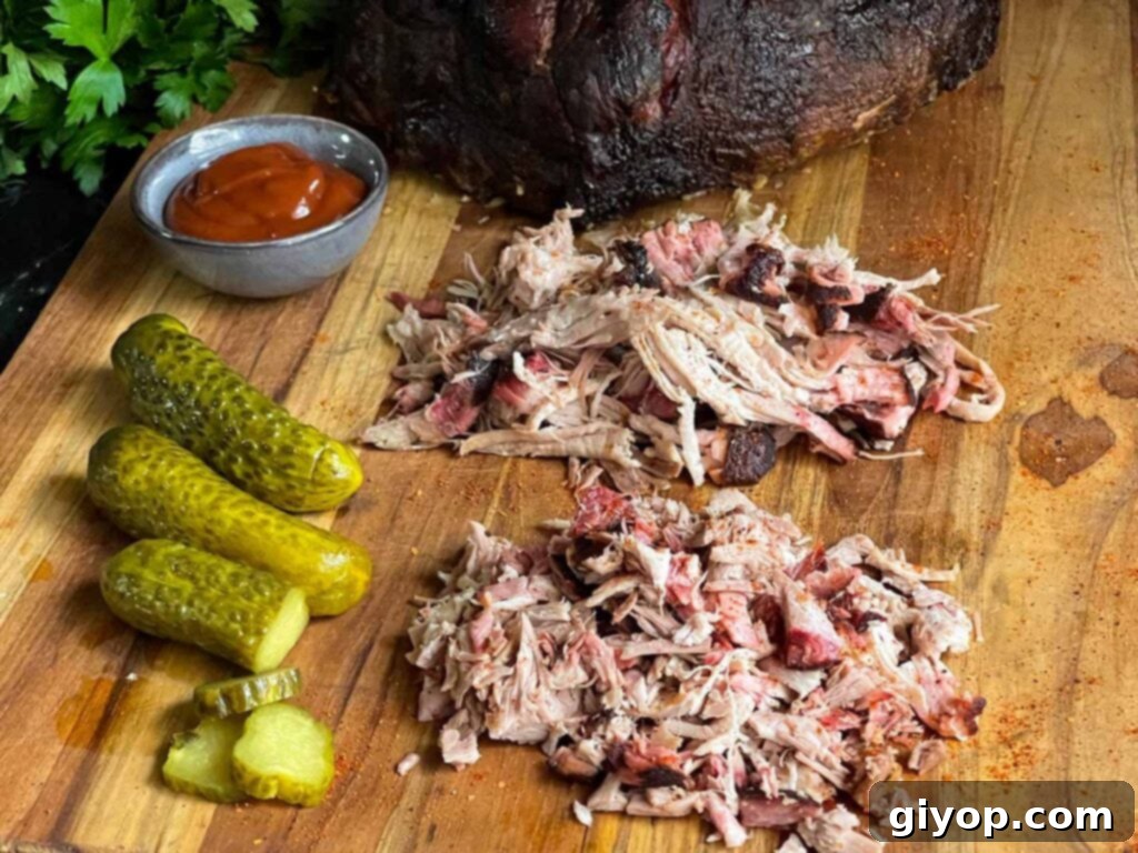 A cutting board laden with both chopped and shredded smoked pork butt, accompanied by pickles and barbecue sauce.