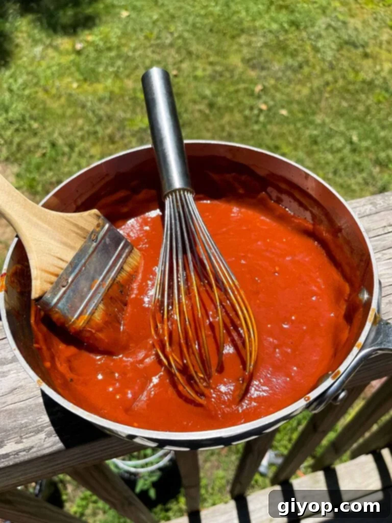 Homemade bourbon chipotle barbecue sauce being whisked in a saucepan, with a basting brush nearby.