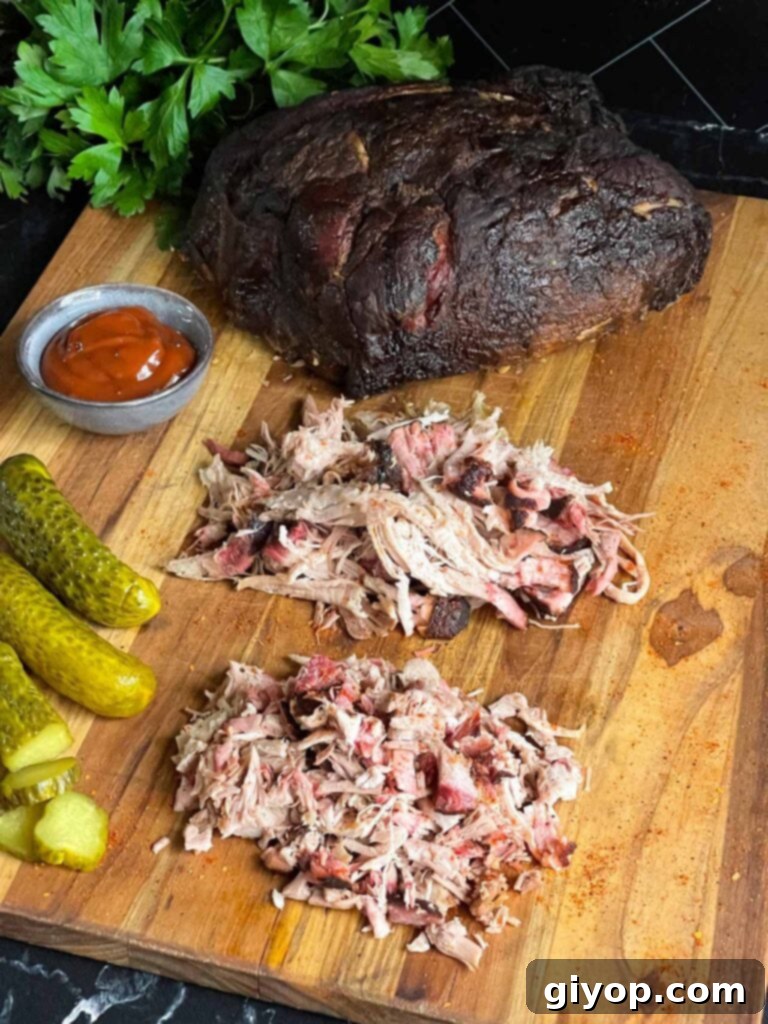 A cutting board showcasing a whole smoked pork butt, alongside piles of shredded and chopped smoked pork butt, demonstrating the versatile results.