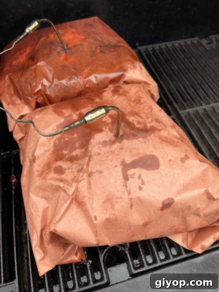 Two pork butts wrapped in butcher paper, continuing to cook on the smoker.