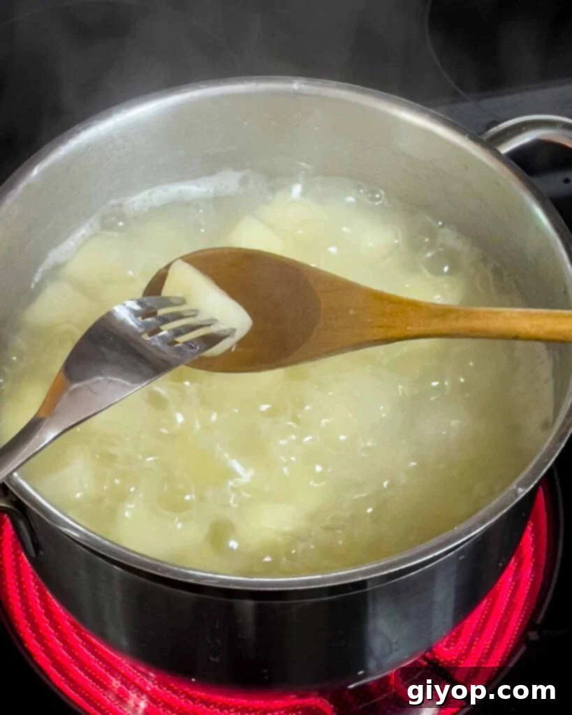 Homestyle Southern Potato Salad 5 A fork is inserted into a boiled potato over the boiling pot.