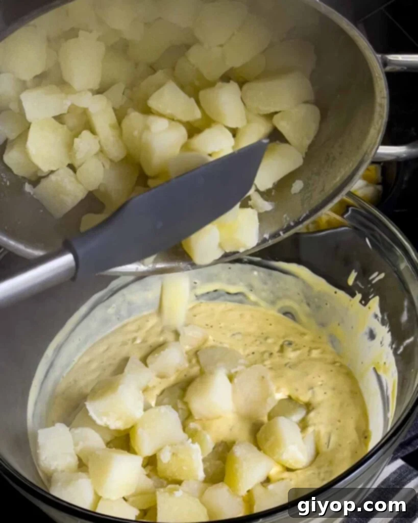 Homestyle Southern Potato Salad 7 Boiled potatoes being added into the Southern potato salad dressing.