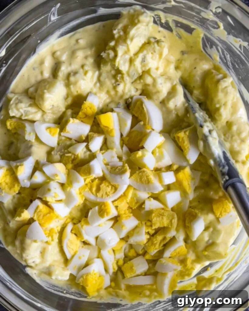 Homestyle Southern Potato Salad 8 Chopped hard-boiled eggs added to the Southern potato salad in a glass mixing bowl.