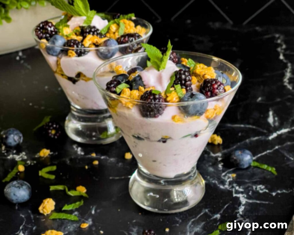 Berry yogurt parfait in a stemless martini glass on a dark surface.