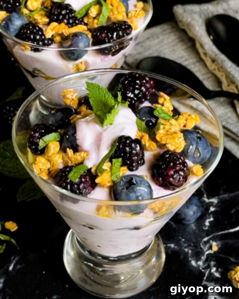 Berry yogurt parfait in a stemless martini glass on a dark surface.